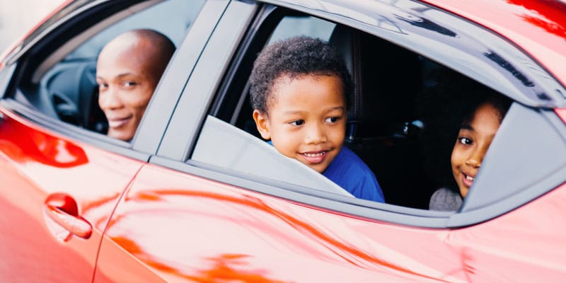 father in driver seat of car with kids in back, windows rolled down and looking out