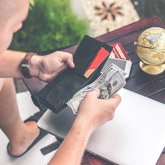 man holding wallet, putting $100 bills inside