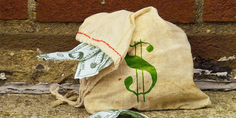 bag of money with a brick wall behind it