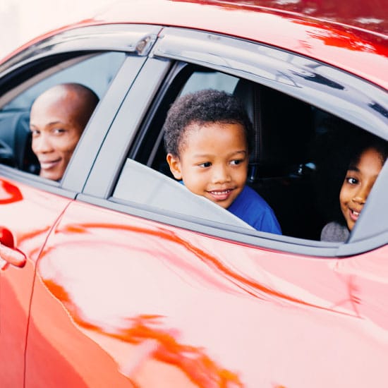 father in driver seat of car with kids in back, windows rolled down and looking out