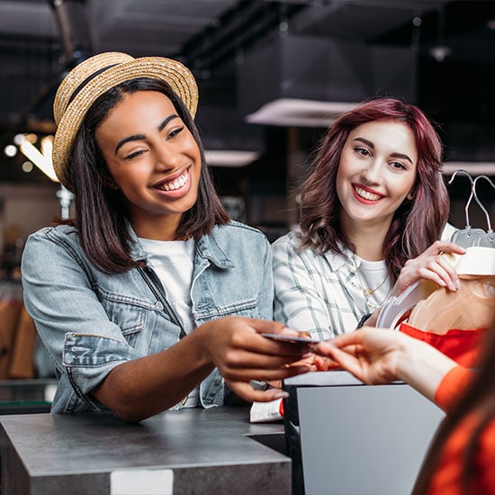 happy women out shopping together, handing card to cashier