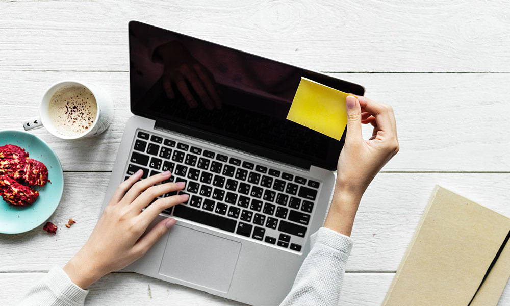 hand reaching to add a sticky note onto a laptop