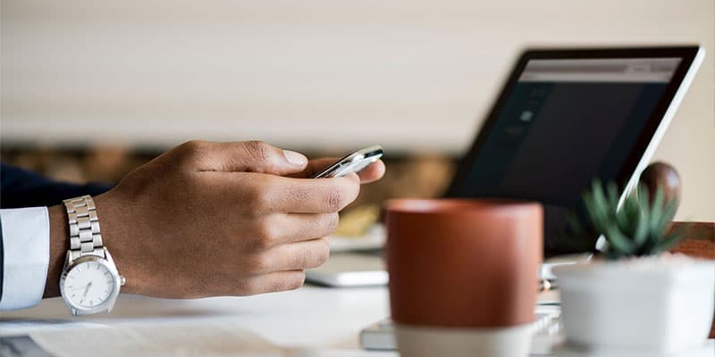 businessman with a watch on his wrist, checking his smartphone; laptop in the background