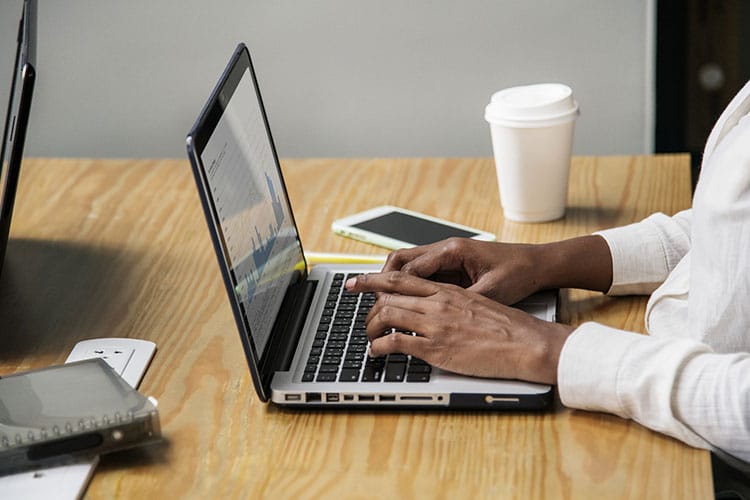 man typing on his laptop at a wooden desk