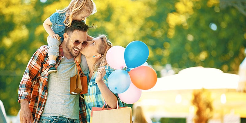 happy family outdoors shopping together, mother holding balloons, father has daughter on his shoulders