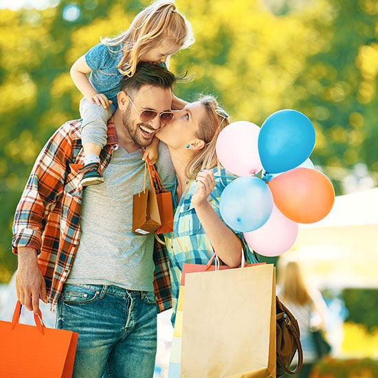 happy family outdoors shopping together, mother holding balloons, father has daughter on his shoulders