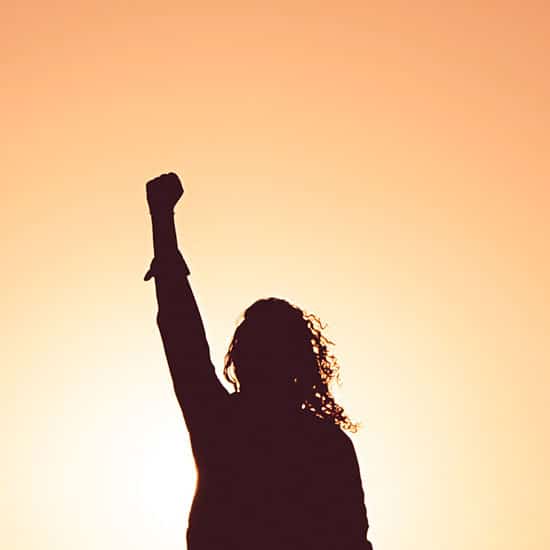 woman's silhouette against the sunset with her fist in the air
