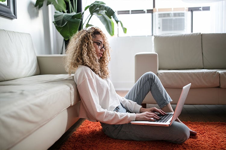 woman sitting on the floor, leaning on couch using laptop