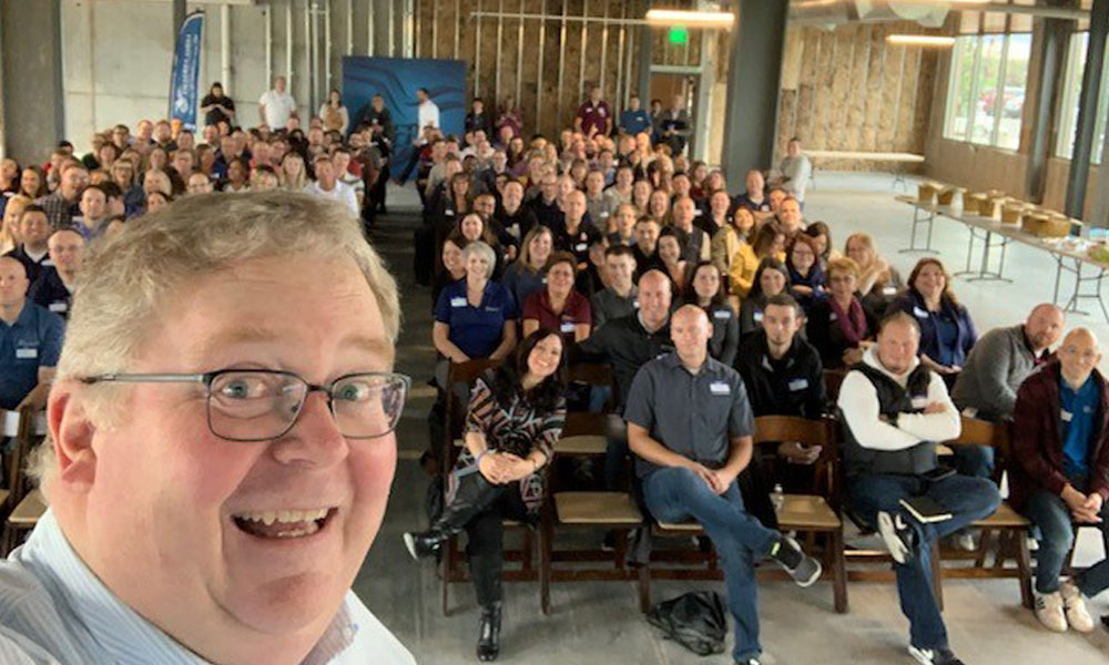 CEO Shane London takes a selfie with rows of other employees in the background