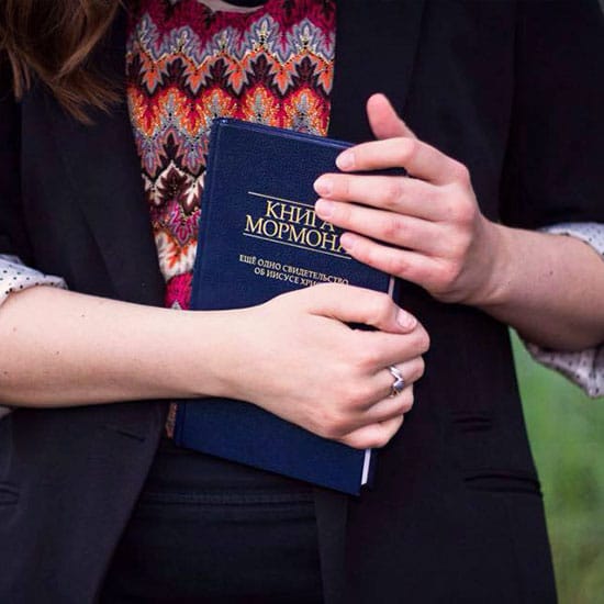 young woman holding a copy of the Book of Mormon in a foreign language