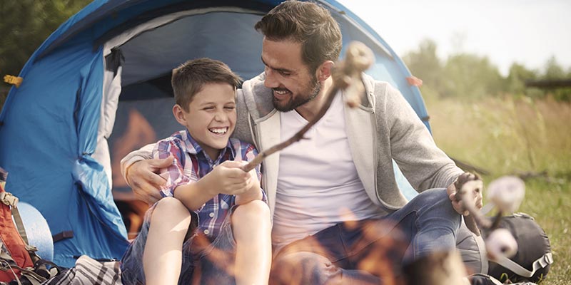 father and son enjoying a camping trip together, roasting marshmallows over a fire