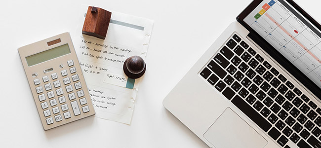 top view of a white desktop with laptop, plant, calculator, and notes