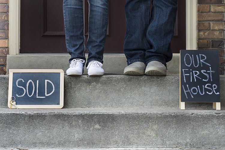 young couple on the steps of their first home with chalkboard signs reading 'sold' and 'our first house'