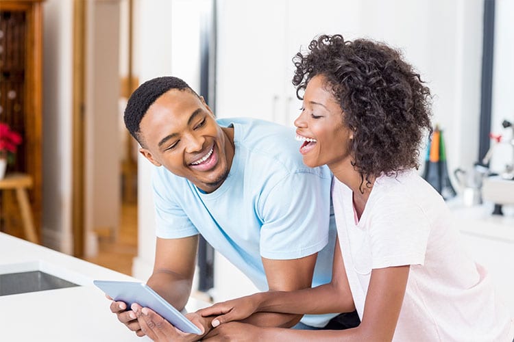 happy couple looking at homes on a tablet in their kitchen