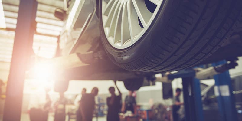 close up of a vehicle lifted up, mechanics inspecting the car in the background out of focus