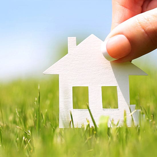 close up of a paper house cutout, fingers holding it in the grass