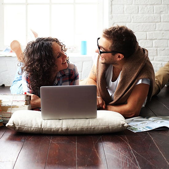 couple on the floor of their apartment looking at a laptop together