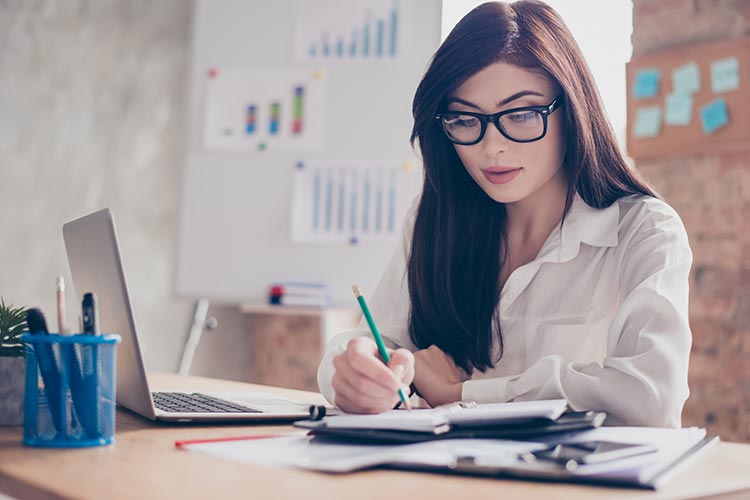 busy professional woman using her laptop and taking notes in a planner