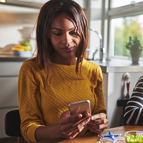 mom checking her phone while working on a craft with daughter