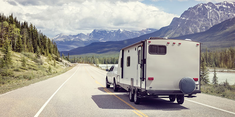 truck pulling a camper trailer up the highway towards the mountains and forest