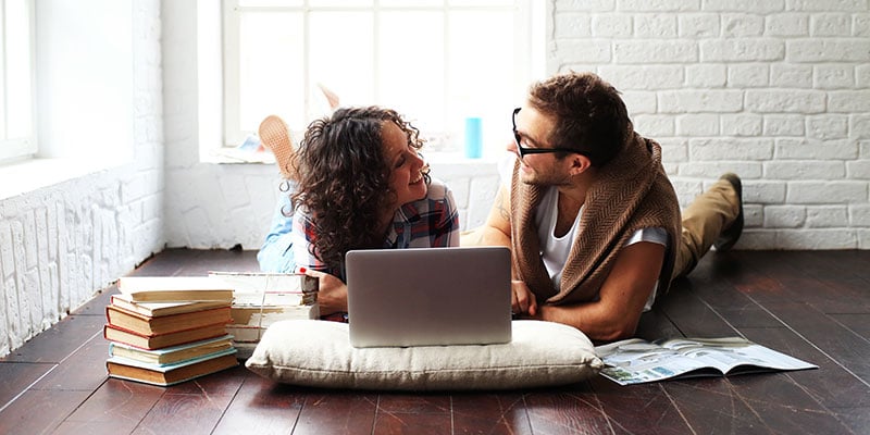 couple on the floor of their apartment looking at homes on a laptop together