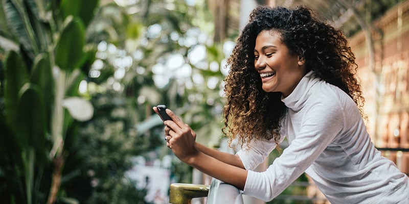 woman on balcony, checking her mobile phone, laughing and smiling