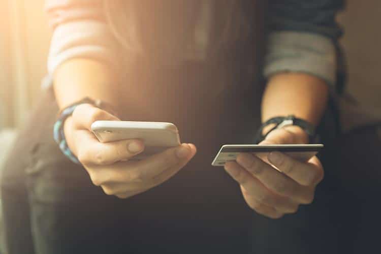 young person holding mobile phone in one hand and debit card in the other