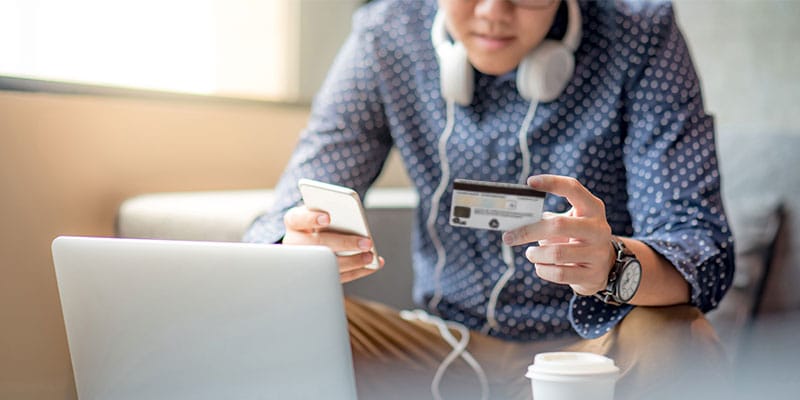 man using his credit card at his laptop, mobile phone in hand