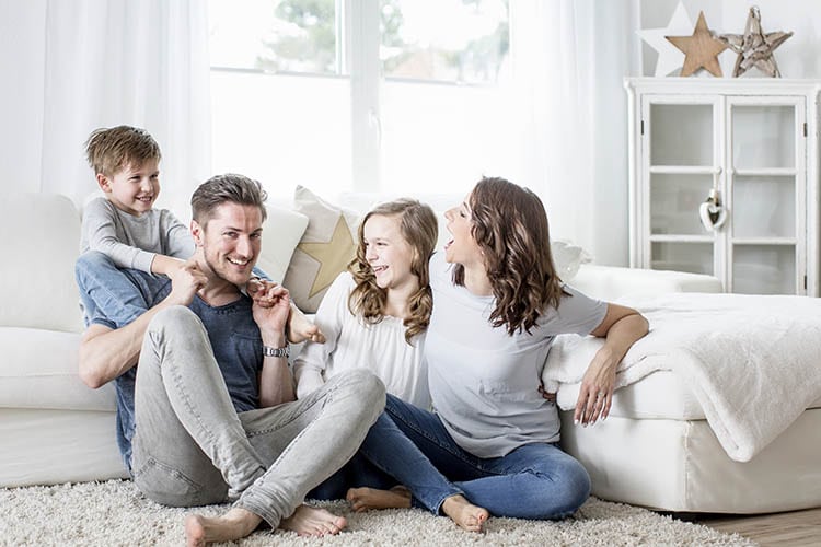 Family of four laughing and playing in the living room of their home