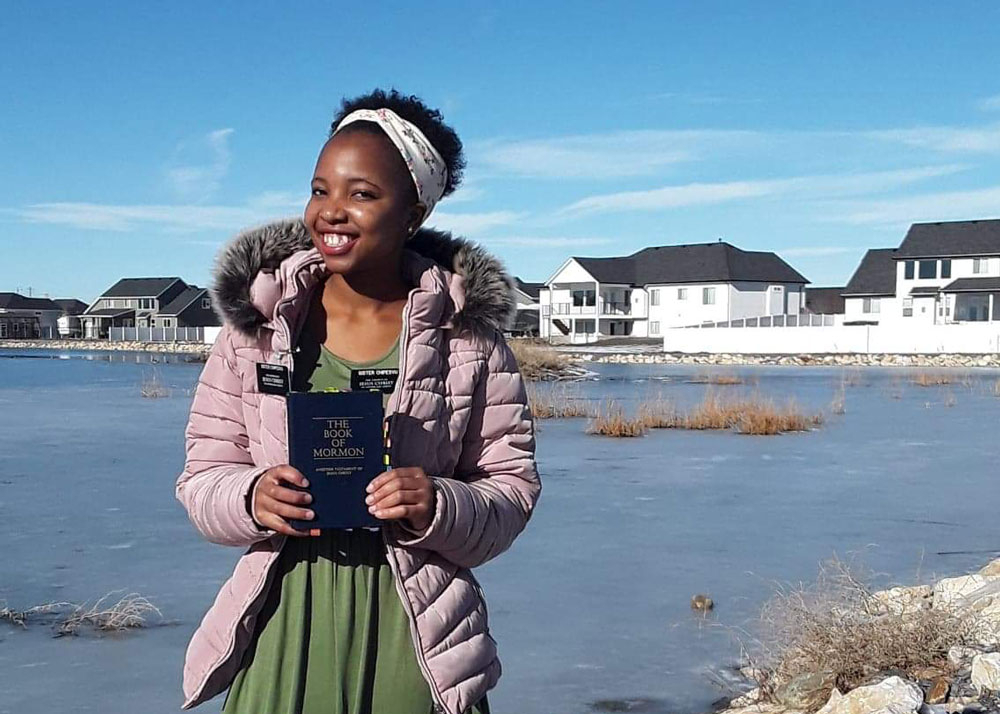 Sister missionary in a winter coat holding a copy of the Book of Mormon.