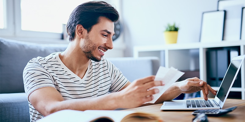 young man looking at his computer and books, learning about finances