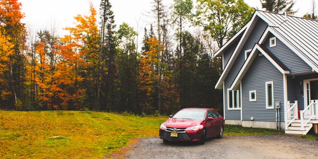 A house and car in front of an autumnal forest.