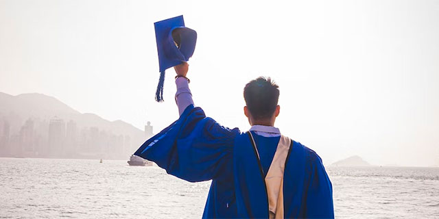 Young man in graduation gown by the ocean.