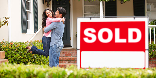 A couple hugging near a home sold sign