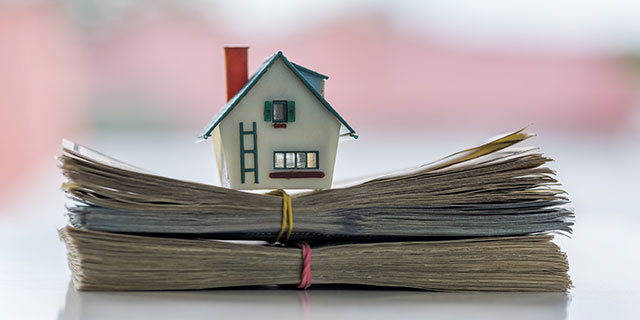 A toy house on top of a stack of bills of money.