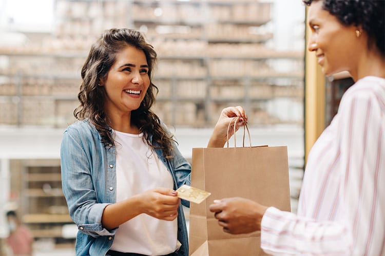 One woman handing her credit card to another woman to pay for her purchase. 