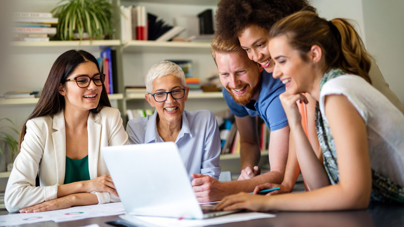 Several employees gathered around a laptop in a cheerful mood