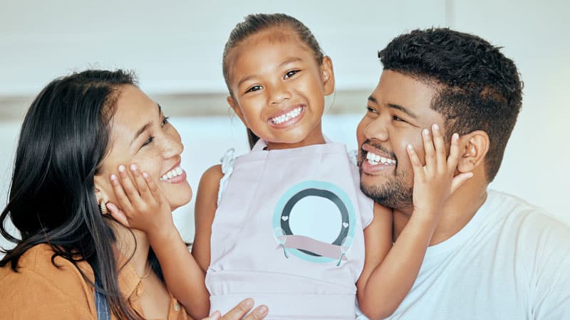 A child with a big smile in between her parents